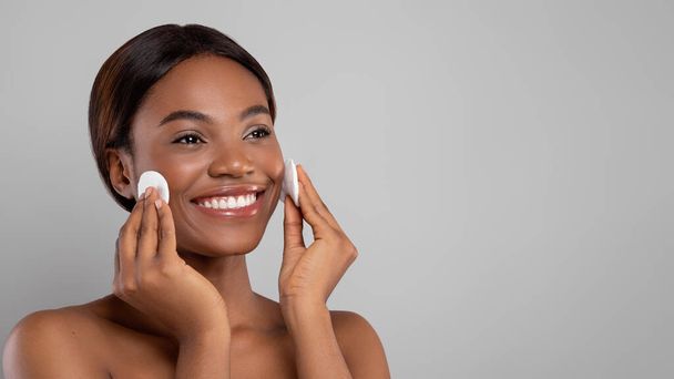 Huidverzorging. glimlachen mooi zwart vrouwelijk reinigen huid met twee katoenen pads - Foto, afbeelding