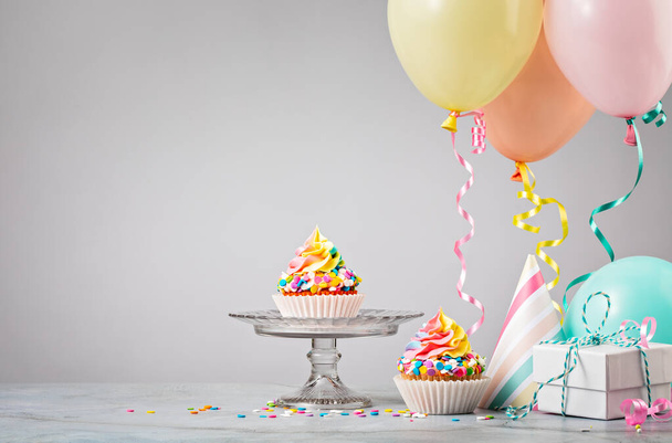 Tęczowe babeczki urodzinowe na imprezie z kolorowymi balonami - Zdjęcie, obraz