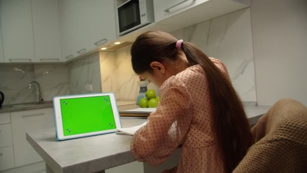 Visão traseira da menina da escola fazendo lição de casa on-line usando tablet dentro de casa - Filmagem, Vídeo