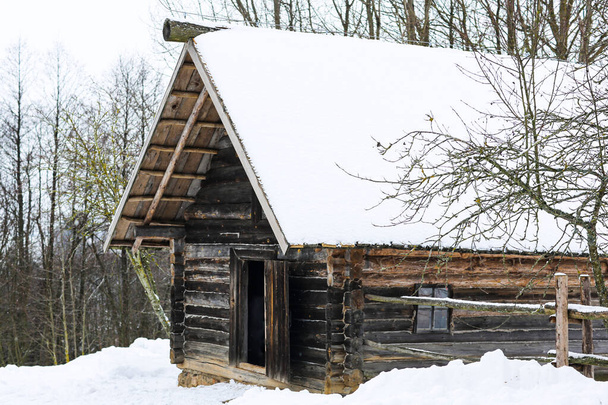 Invierno paisaje ruso. Una vieja choza de madera, una casa de troncos con techo de paja. Pueblo ruso abandonado cubierto de nieve. Casa de troncos con granero. - Foto, imagen