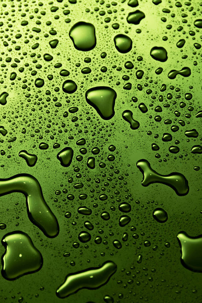 Green metal water drops on dark reflective surface - 写真・画像