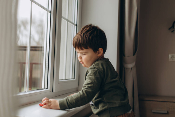 boy in a green shirt lying and playing toy cars on the windowsill. - Foto, afbeelding