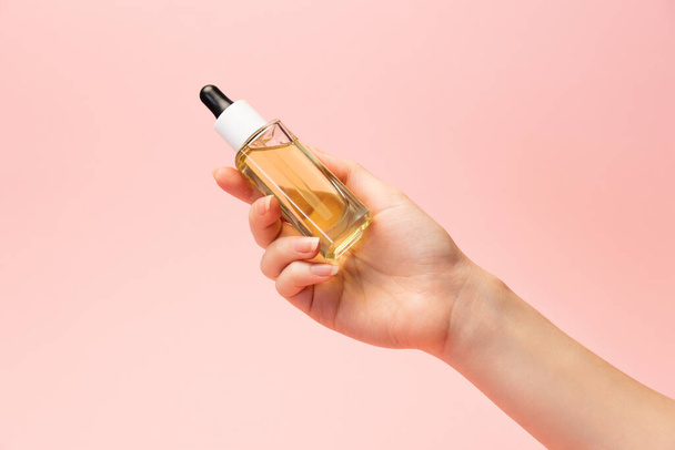 Skin care. Beautiful female hand hold a glass bottle of care cosmetics with a pipette. Pink background. The concept of beauty products. - Zdjęcie, obraz
