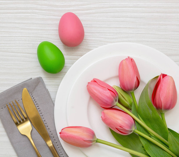 Easter place setting. Pastel color egg and pink tulip flower decoration on white wooden background, view from above. Spring Holiday celebration. - 写真・画像