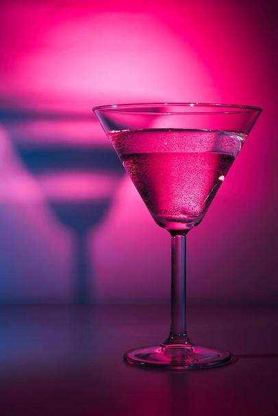 Martini cocktail drink with ice cubes in neon iridescent pink and blue colors. Minimal night party life and Juzz concept. Background painted with light - Foto, Imagen
