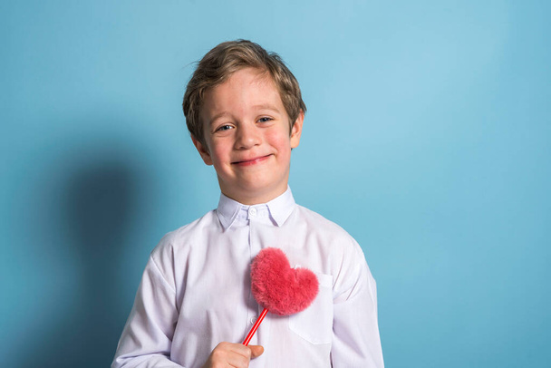 a European boy in a white shirt holds a fluffy red heart in his hands - Foto, Imagen