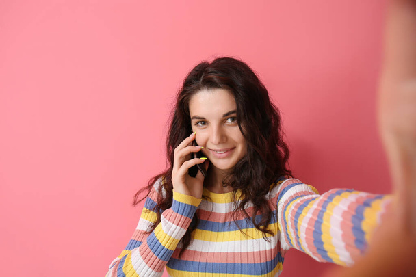 Krásná brunetka žena mluví mobilním telefonem na růžovém pozadí - Fotografie, Obrázek