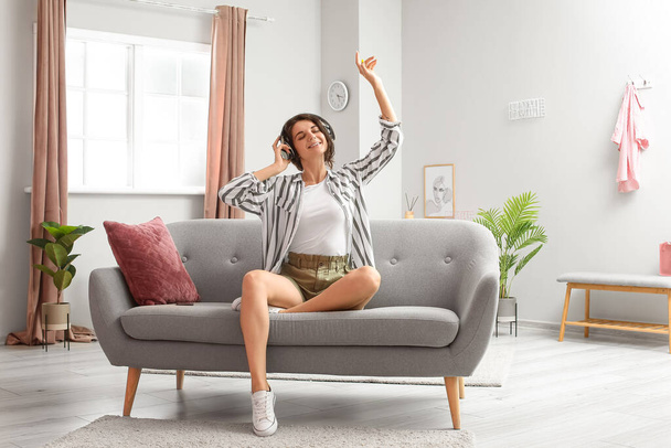 Beautiful brunette woman in headphones listening to music on sofa at home - Φωτογραφία, εικόνα