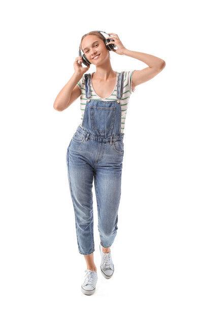 Young woman in denim jumpsuit with headphones on white background - Foto, afbeelding