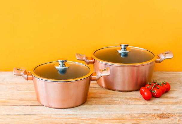 Copper cooking pots and tomatoes on wooden table against orange background - Photo, Image