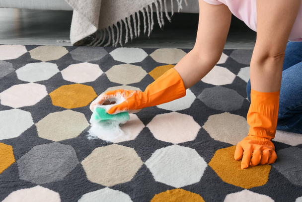 Ama de casa en guantes de goma limpieza de alfombras de colores con esponja en casa - Foto, imagen