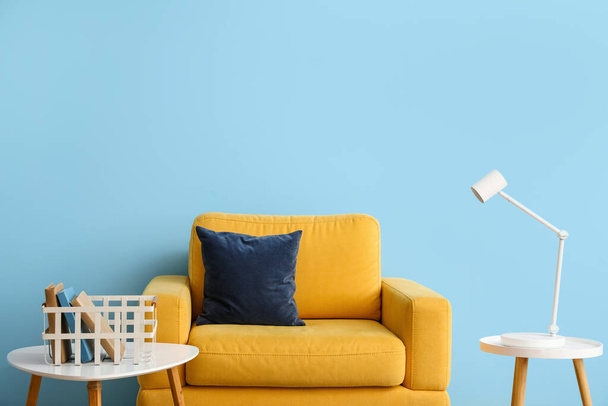 Sárga fotel, dohányzóasztal könyvekkel és lámpával a kék fal mellett - Fotó, kép