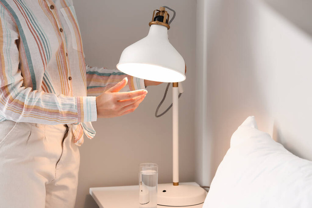 Woman changing light bulb in lamp near bed at home - Photo, Image
