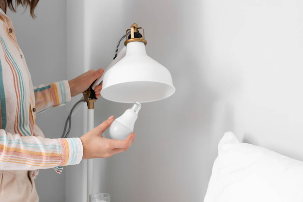 Mujer cambiante bombilla en lámpara cerca de la cama en casa - Foto, imagen