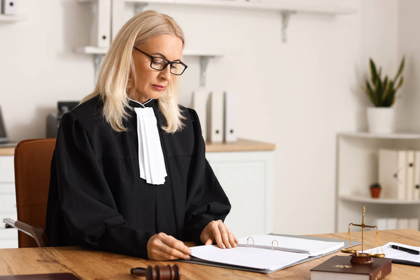 Зріла жінка-суддя, що працює з документами за столом у залі суду
 - Фото, зображення