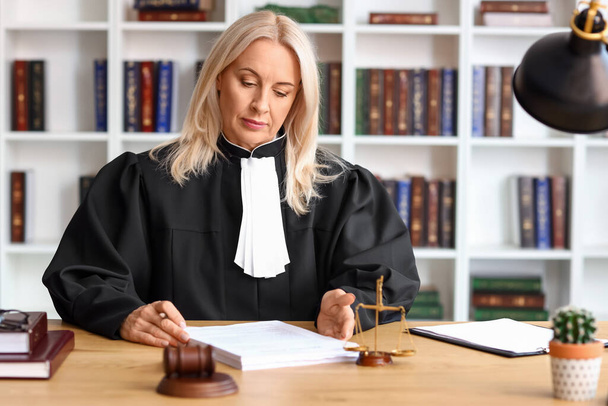 Juez mujer madura trabajando con documentos en la mesa en la sala del tribunal - Foto, imagen