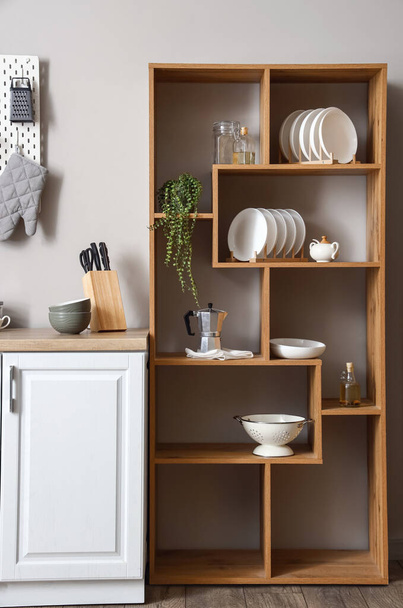 Wooden shelving unit with dishware, coffee maker and houseplant near light wall in kitchen - Photo, Image