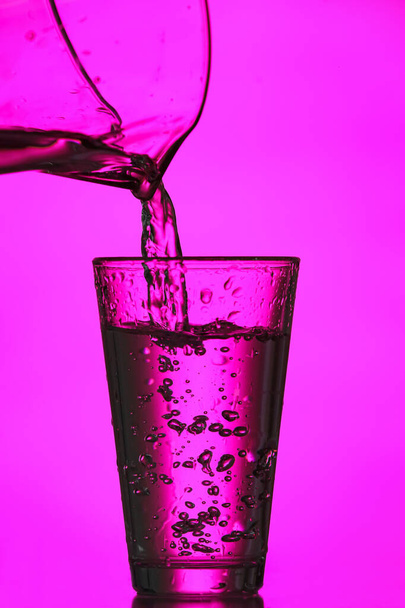 Gieten van helder water in glas op kleur achtergrond - Foto, afbeelding