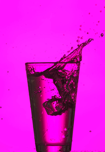 Vaso de agua clara con salpicadura sobre fondo de color - Foto, Imagen