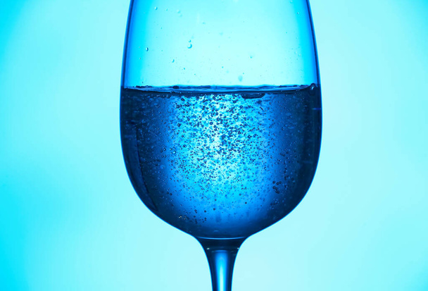 Glass of clear water on blue background - 写真・画像