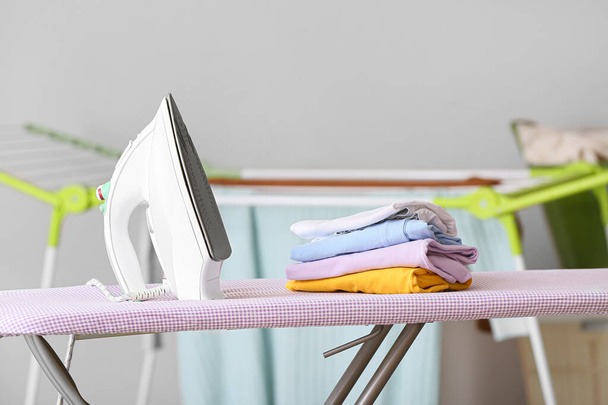 Electric iron and stack of clean clothes on board - Photo, Image