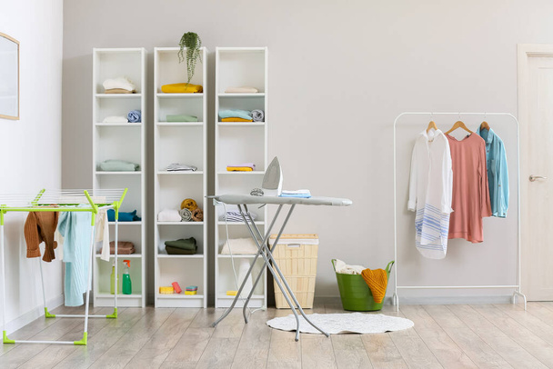Interior of modern laundry room with ironing board and shelf units with different clothes - Photo, image