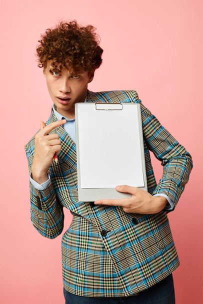 Young curly-haired man in a plaid jacket copy-space folder pink background unaltered - Φωτογραφία, εικόνα