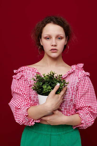 Young woman standin and holding flower in pot red background unaltered - Фото, зображення