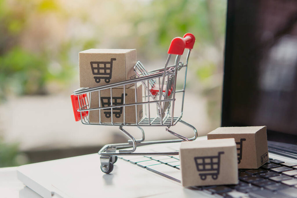 Online einkaufen. Karton mit einem Warenkorb-Logo in einem Einkaufswagen auf der Laptop-Tastatur. Shopping-Service im Internet. bietet Hauszustellung - Foto, Bild