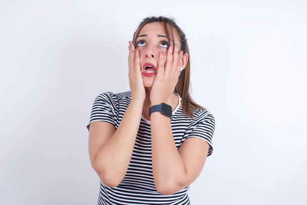 young Arab woman wearing striped t-shirt over white background keeps hands on cheeks has bored displeased expression. Stressed hopeless model - Photo, Image