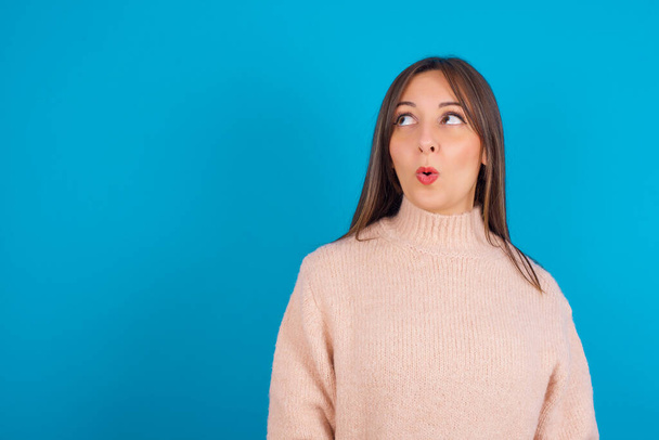 Shocked Young arab woman wearing knitted sweater over blue backgtound look empty space with open mouth screaming: Oh My God! I can't believe this. - Photo, Image