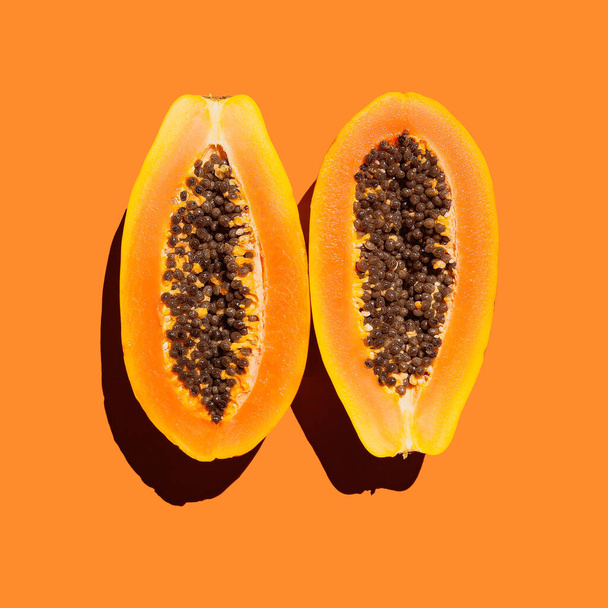 Rijp papaya in de snede, twee helften op een oranje achtergrond, hard licht, geïsoleerd - Foto, afbeelding