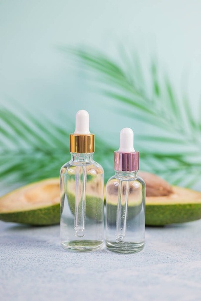 garrafa de vidro com um produto cosmético com uma pipeta para cuidados com a pele no fundo de uma folha de palma com abacate - Foto, Imagem