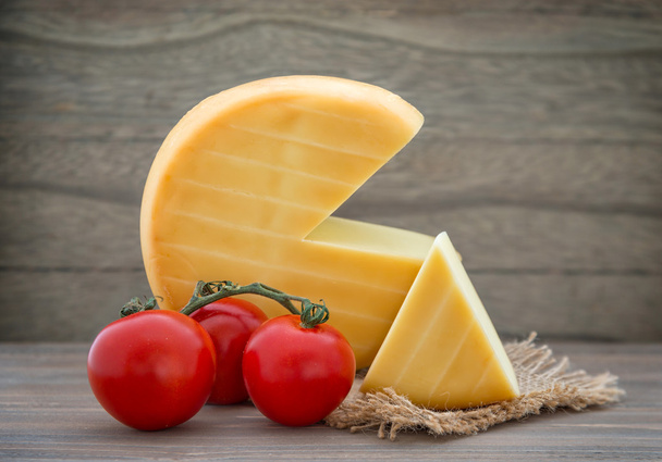 Rueda de queso ahumado, tomates sobre mesa de madera
 - Foto, imagen