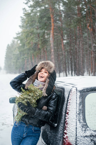 Çam ağacıyla gülümseyen güzel kadın dışarıda eğleniyor. Karlı ormandaki kadın. Kış tatili. - Fotoğraf, Görsel