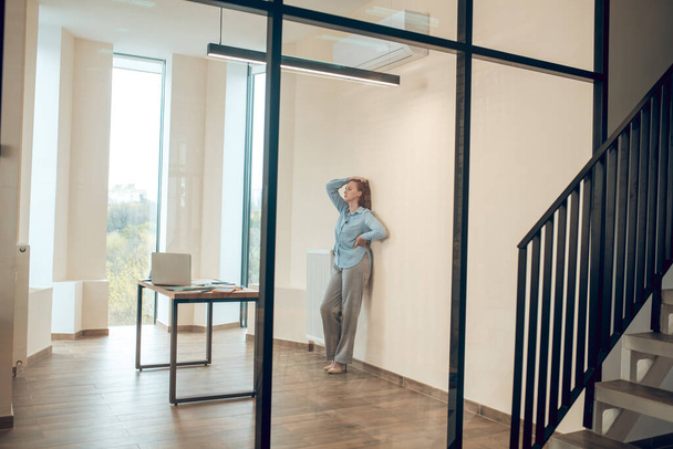 Tired woman standing leaning against wall in office - Foto, Bild
