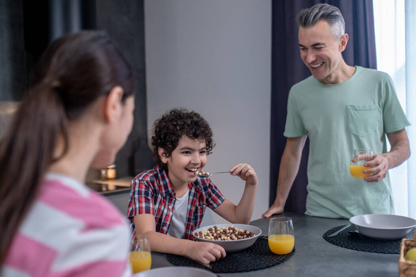 Man looking at boy eating cereal at table - Foto, afbeelding