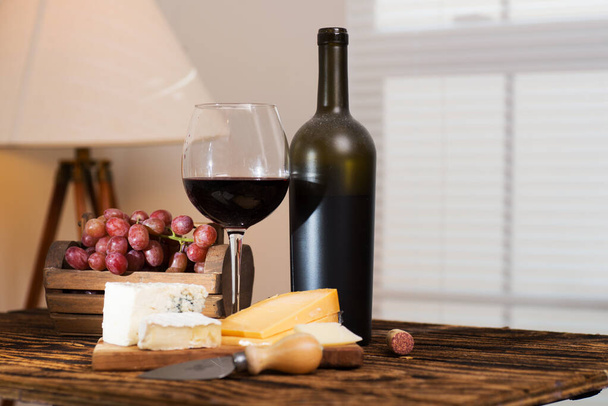 Tahta masada peynirli ve üzümlü kırmızı şarap. - Fotoğraf, Görsel