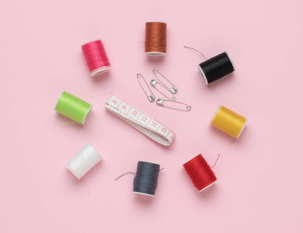 ピンクの背景にテープ、ピン、およびマルチカラースレッドのセットを測定します。家庭の針仕事と刺繍の概念。平敷. - 写真・画像