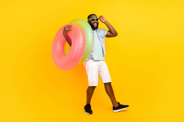 Full length body size view of attractive trendy cheery guy carrying life buoy having fun isolated over bright yellow color background - Zdjęcie, obraz