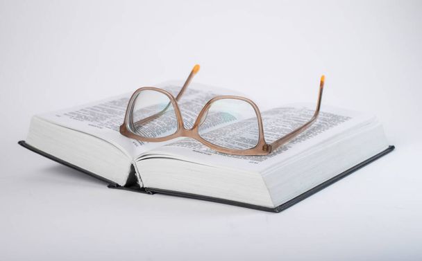 Eyeglasses at open book. Education and religious study concept. Bible, dictionary reading.  - 写真・画像