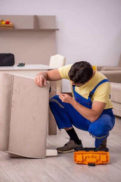 Young male carpenter repairing arm-chair at home - Fotoğraf, Görsel