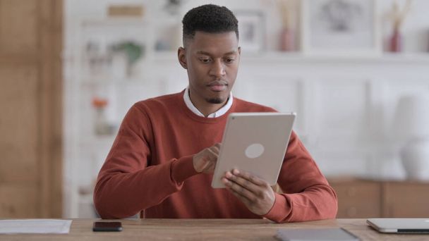 Αφρικανικός άνθρωπος που χρησιμοποιεί tablet ενώ κάθεται στο γραφείο - Φωτογραφία, εικόνα