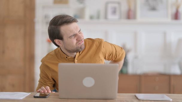 Young Man having Back Pain while using Laptop in Office - Foto, Bild