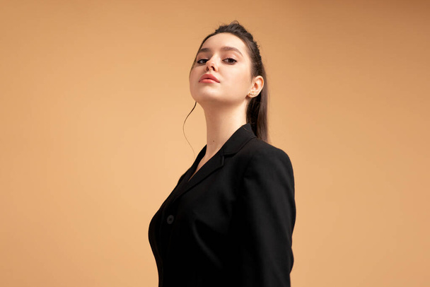 Young business woman close up portrait dressed black jacket standing studio isolated on color background. Caucasian female business person looking at camera with serious face. Medium shoot - Fotó, kép