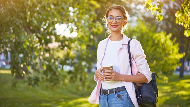 Businesswoman standing summer park Business person Outdoors Successful european caucasian woman freelancer or teacher walking outside with black backpack dressed denim jeans white shirt pink jacket - Photo, Image