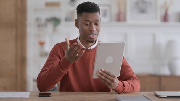 アフリカ人男性がオフィスでタブレットでビデオ通話を行う - 写真・画像