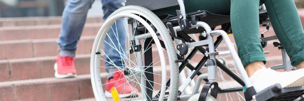 Adam merdivenlerde bir kadınla birlikte tekerlekli sandalyeyi kaldırıyor. - Fotoğraf, Görsel