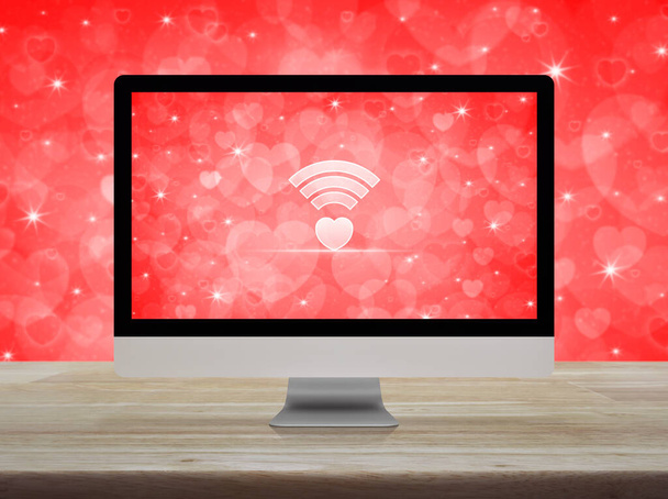 Heart love wifi flat icon on desktop modern computer monitor screen on wooden table over blur red love wall, Internet online love connection, Valentines day concept - Photo, Image