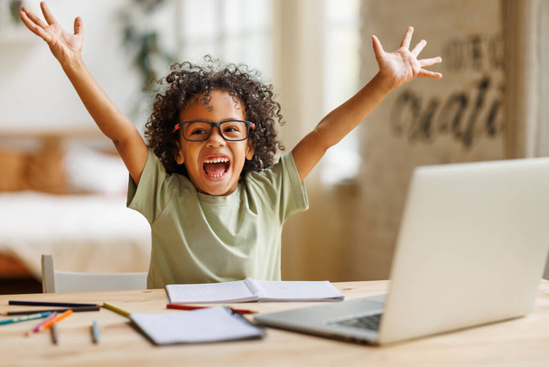 Little african american school boy raising hands up with excitement during home distance education - Φωτογραφία, εικόνα
